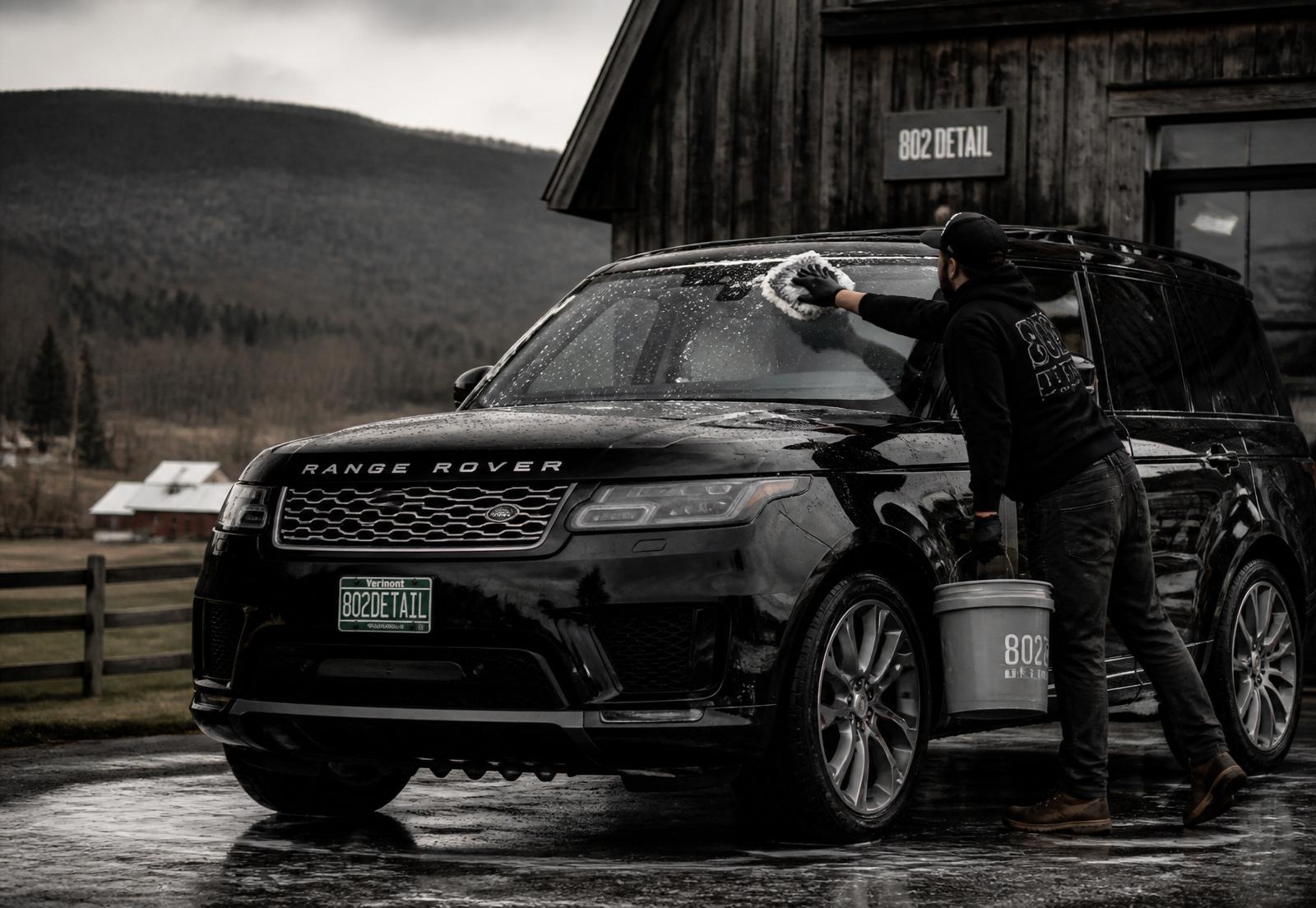 Detailer hand-washing a glossy black SUV outside a barn in rural Vermont